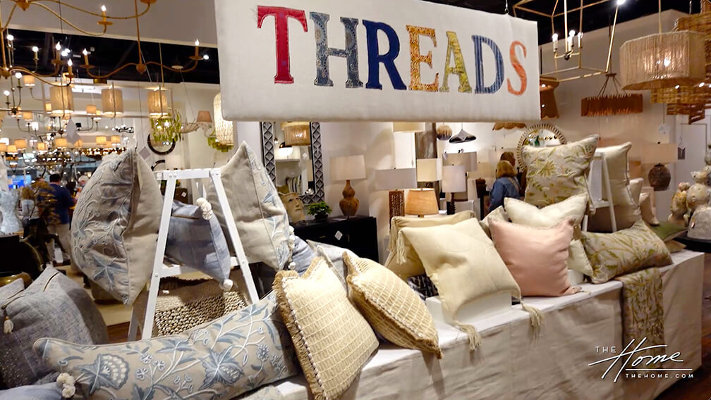 Home decor showroom with large banner with Threads written on it, pillows below on a table