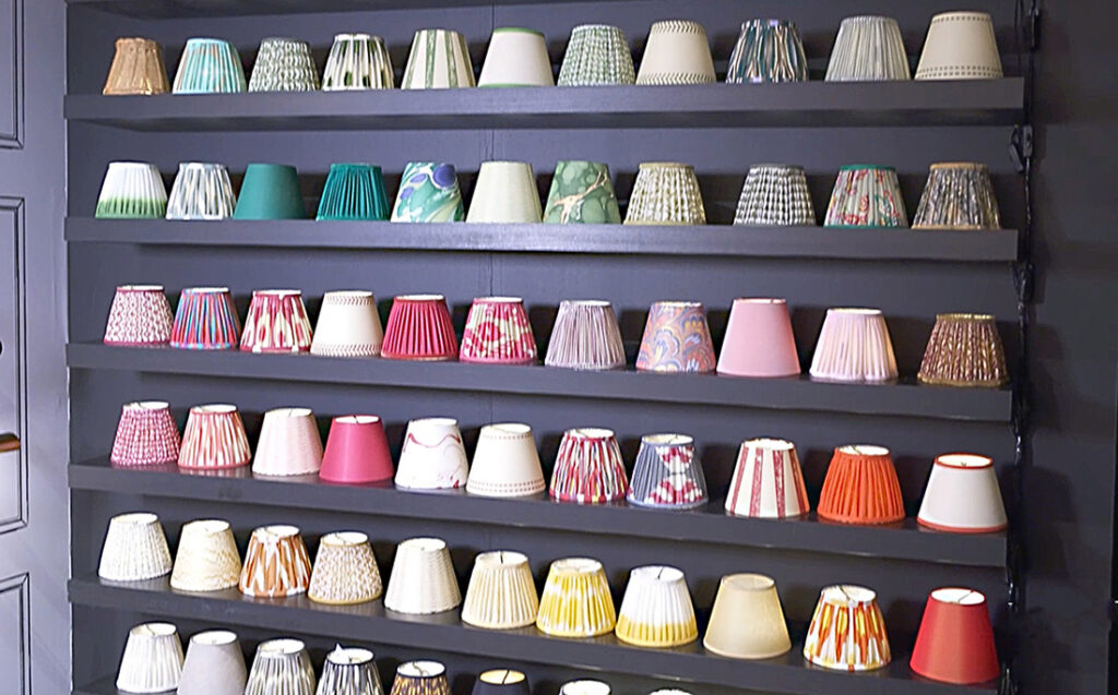 Image: gray wall with six shelves holding dozens of multicolored lampshade choices