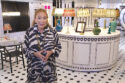 image of woman in zebra stripe dress in front of round table holding many lamps of colors and styles, background has black and white graphic accents