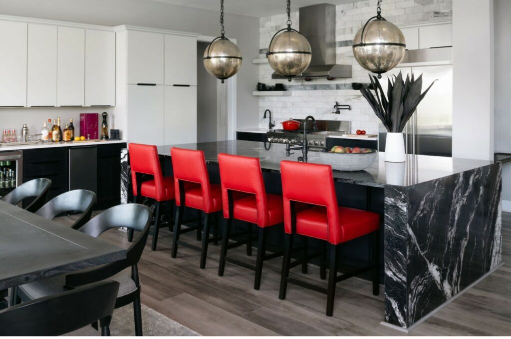 Image: luxury kitchen with black marble island and 4 bright red barstool chairs, white cabinetry, disco ball island lighting