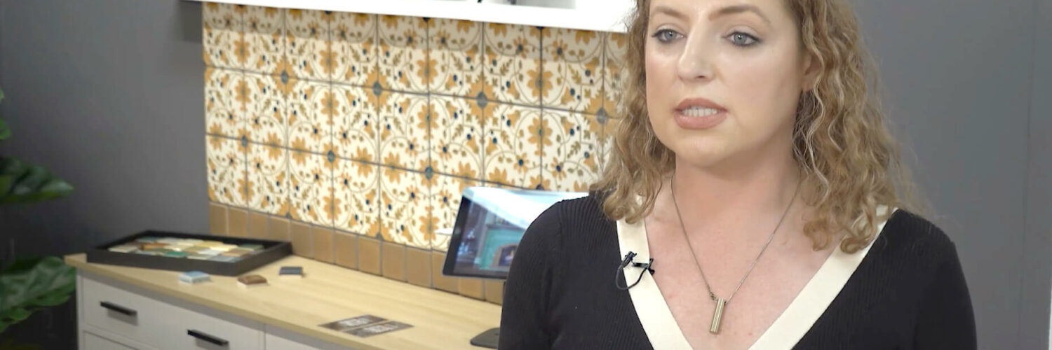 Image: woman in black and white dress in front of art tiles on backsplash in geometric yellow and brown pattern