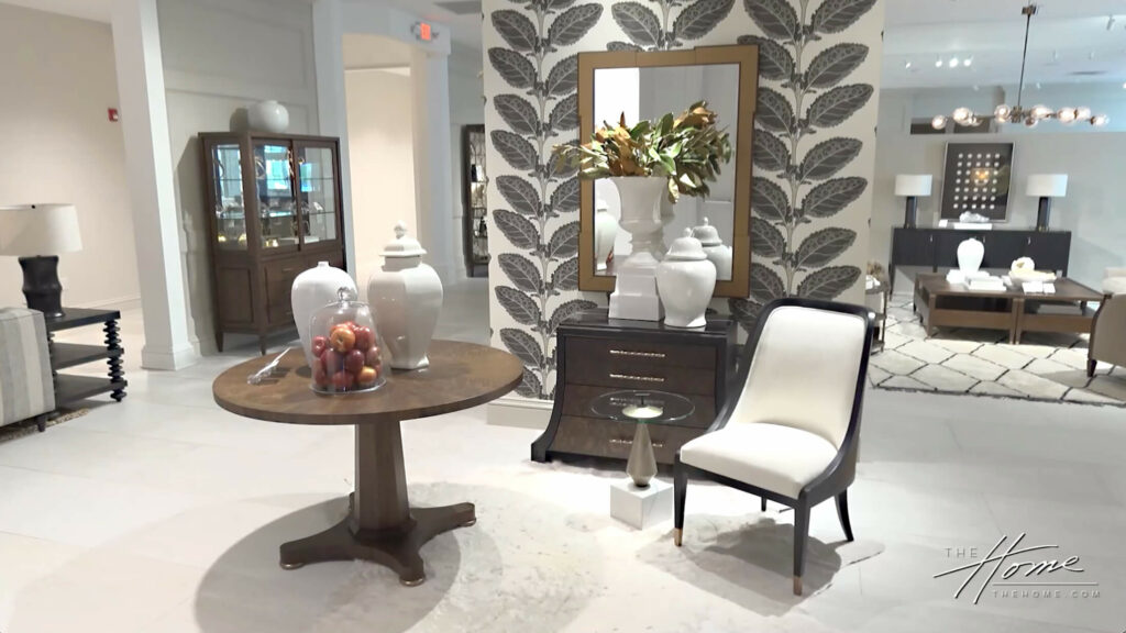 Image: large room with traditional chair, circular wood table and large mirror with feather wallpaper