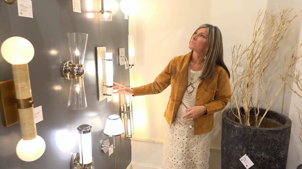 Image of interior designer Debbe Daley wearing suede western jacket inspecting lighting in Currey and Co. showroom