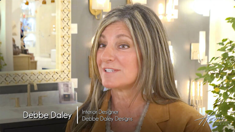 Image: smiling woman in tan suede jacket and beaded blouse in Currey Co. lighting showroom Text: Debbe Daley Designs Design Industry Leader and Educator