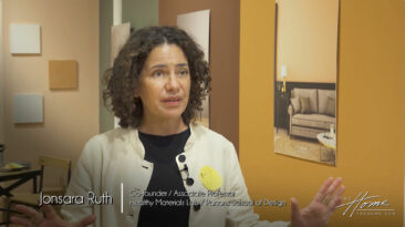 Image of woman with dark curly hair and white jacket over black top in room with warm paint colors on wall