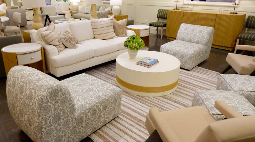 Image: furniture showroom with living room display, cream couch, round white coffee table, side chairs with pattern, beige and tan striped rug