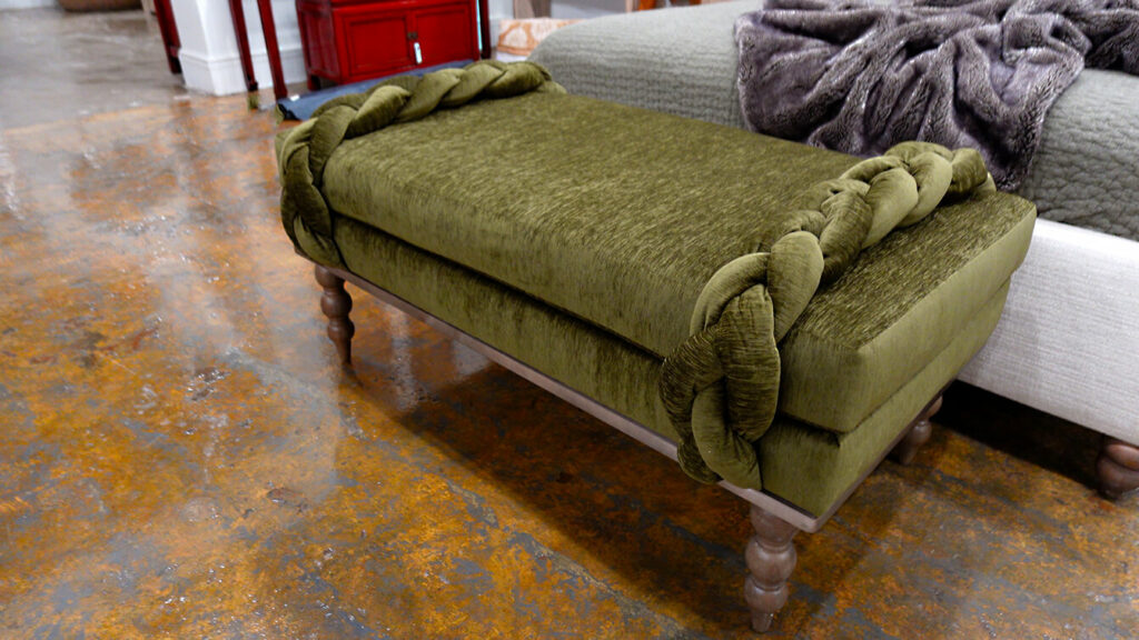 Image: green velour upholstered bench with braid decor on each end at food of white bed, on stained concrete floor