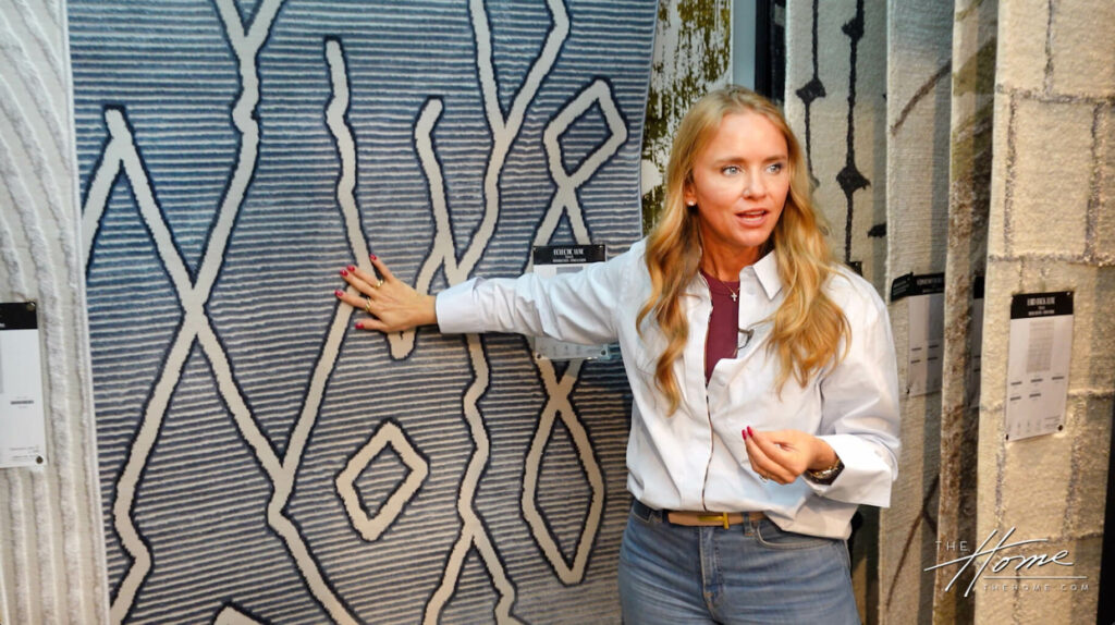 Image: woman with blonde hair and white button shirt holding arm outstretched to blue and white abstract rug