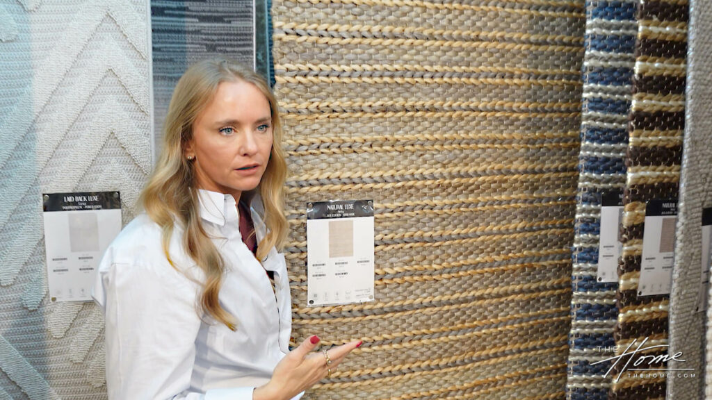 Image: blonde woman Tamara Day holding a beige and green textured woven rug in rug showroom
