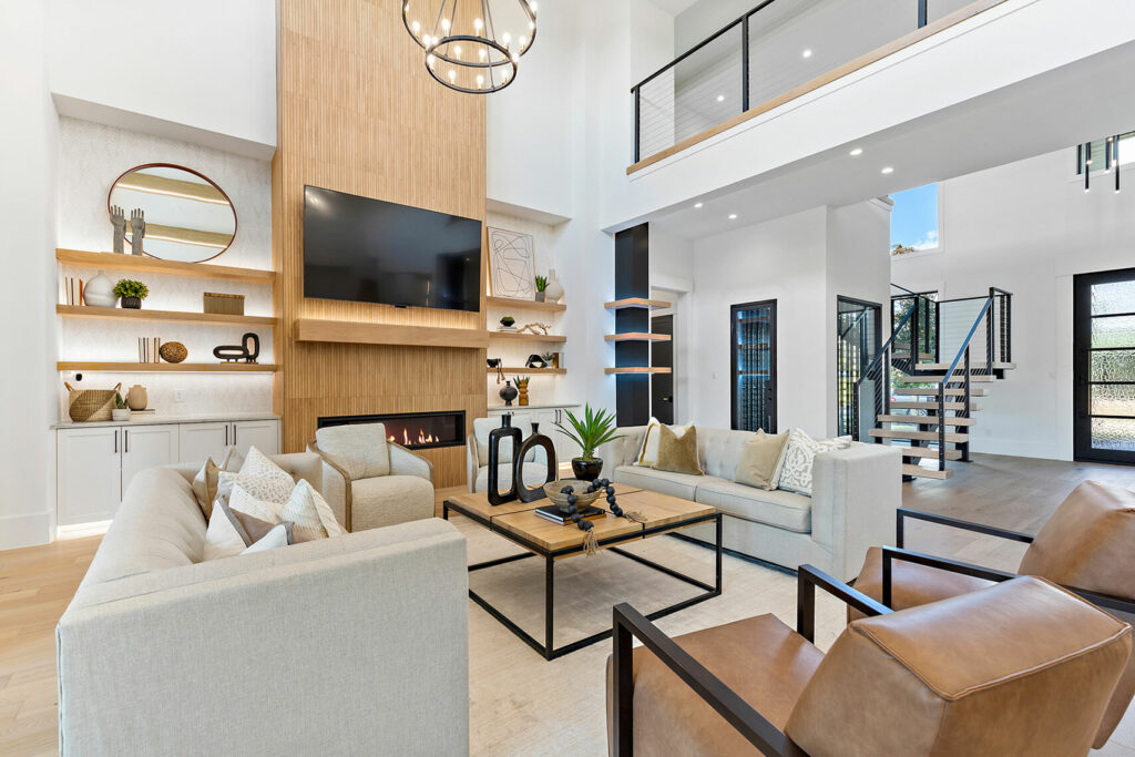 Image: white living room with wood panel fireplace, beige sectional sofa, leather arm chairs, square wood and iron coffee table