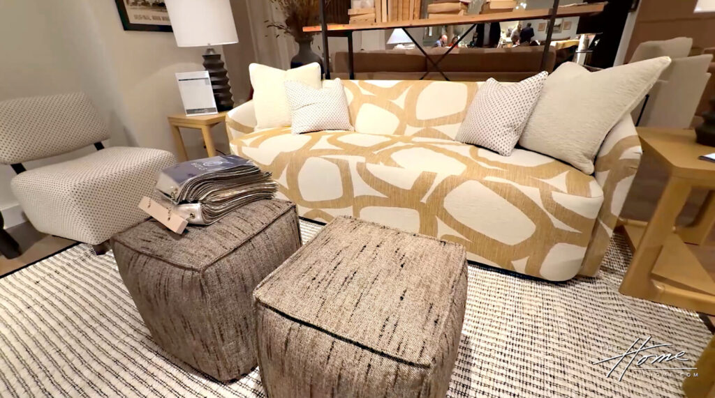 Image: cream modern sofa with bold abstract ache pattern on black and white striped rug, gray flecked pouf ottomans, side chair and lamp