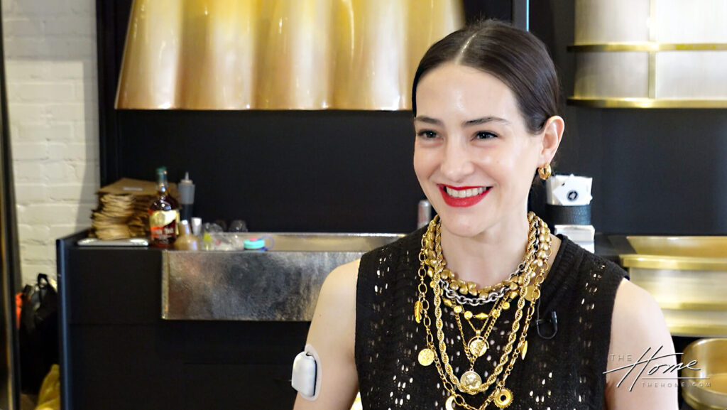 Image: smiling Hispanic woman, Alejandra Thompson de Jordan of Thompson Traders in black dress and gold jewelry with satin brass range hood in background