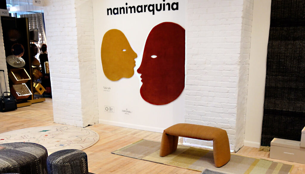 Image: nanimarquina rugs showroom with Jaime Hayon ochre rug and brown rug woven as faces talking, small wool bench, white brick wall
