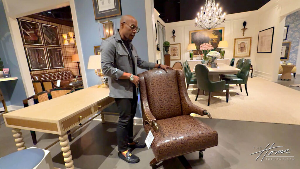 Corey Damen Jenkins in gray shirt shows off Hancock & Moore leather Doxon office chair with horse head finials on arms, next to tan desk and dining table with green Brielle chairs