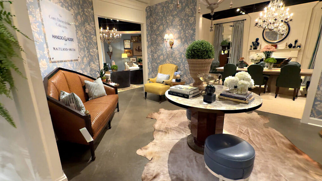 Corey Damen Jenkins foyer design with Maitland-Smith bespoke accessories, brown leather couch, tan animal hide rug, blue footstool, floral wallpaper, accent table with plant and decorative items